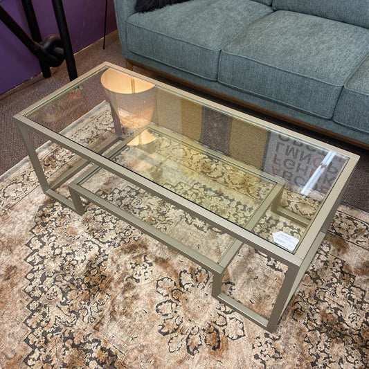 Glass coffee table with a lamp on a patterned rug in a living room setting.