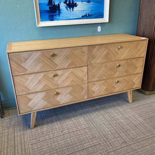 Wooden dresser with a herringbone pattern against a blue wall.