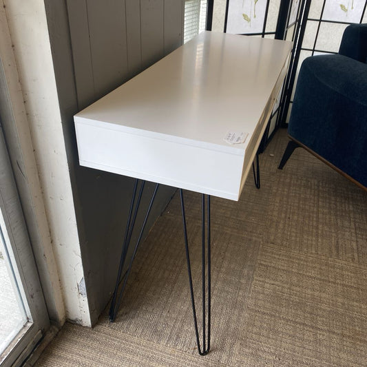 White desk with black hairpin legs in a room with a window and chair.