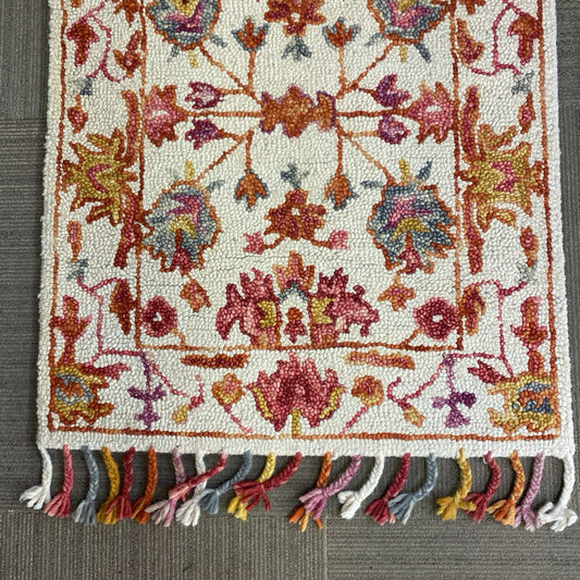 Decorative rug with colorful floral patterns and tassels on a gray surface