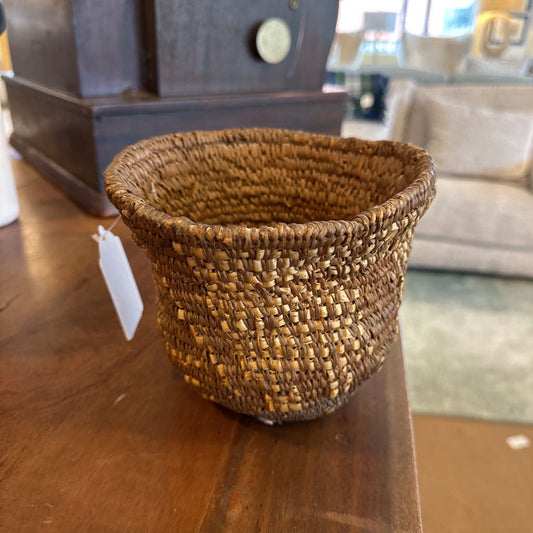 Woven basket on a wooden surface with a tag, in an indoor setting.