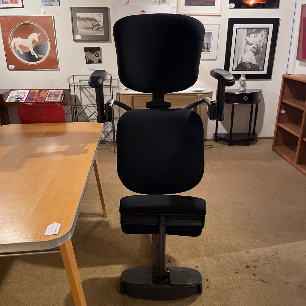 Black office chair in a room with a table and framed pictures on the wall.