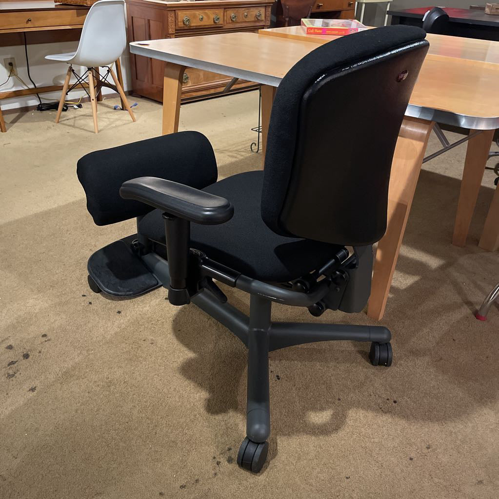 Black office chair in a room with a desk and chairs.