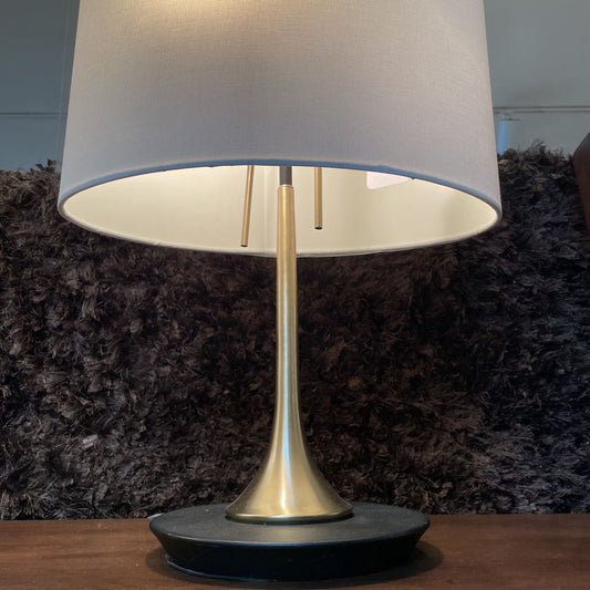 Table lamp with a white shade and gold base on a wooden surface.