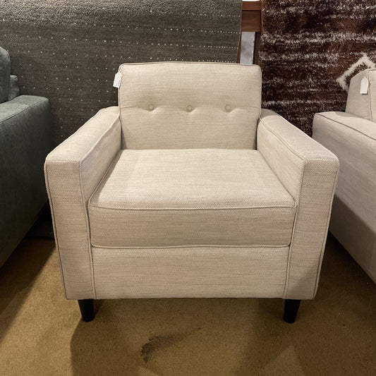Beige armchair in a showroom setting with textured walls and flooring.