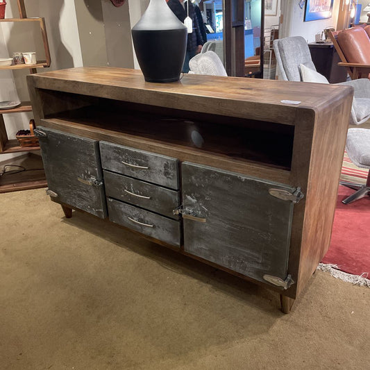 Wooden console table with metal doors and drawers in a room setting.