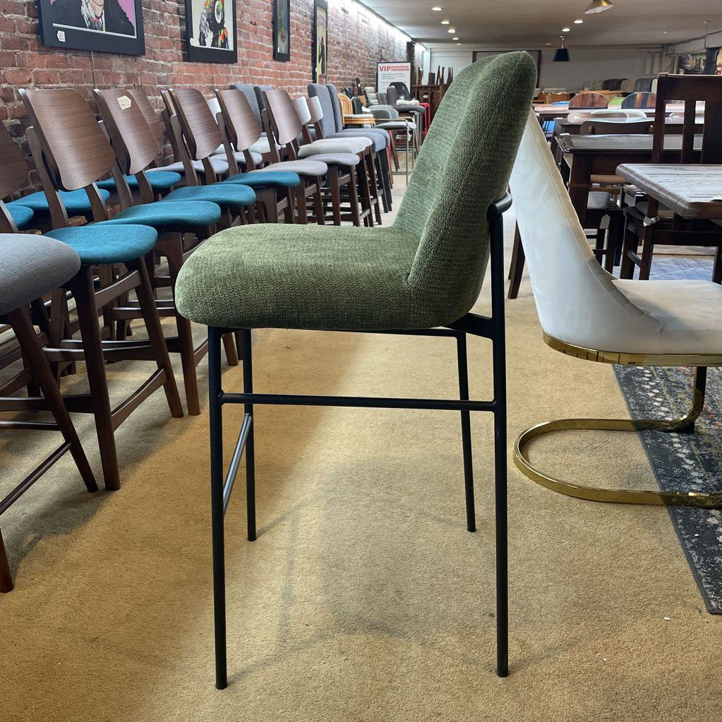 Green bar stool with black legs in a room with other chairs and tables.