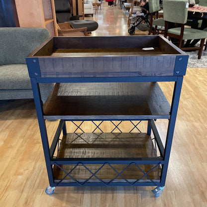 Three-tiered metal cart with wooden shelves on a wooden floor.