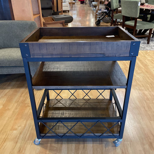 Three-tiered metal cart with wooden shelves on a wooden floor.