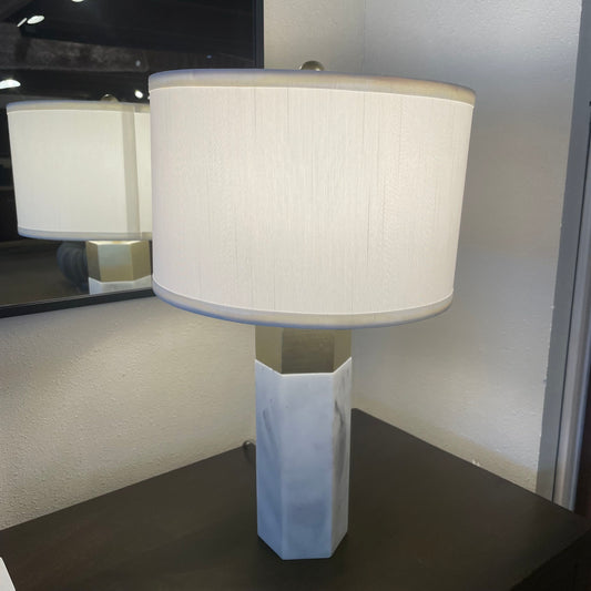Table lamp with a white shade on a dark surface, reflected in a mirror.