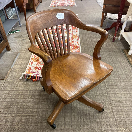 Wooden office chair on a carpeted floor with a rug and furniture in the background