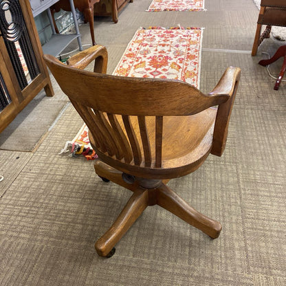 Wooden swivel chair on a carpeted floor with other furniture items in the background.