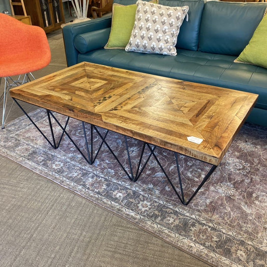 Wooden coffee table with metal legs in front of a blue sofa with green and patterned cushions.