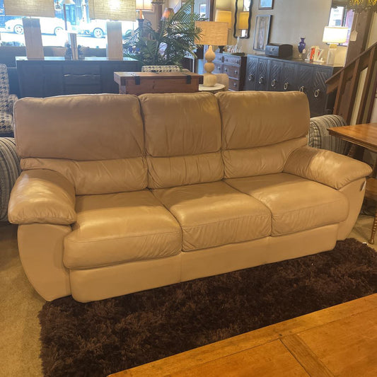 Beige leather sofa in a room with a rug and furniture.