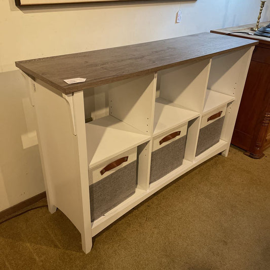 White storage console with wooden top and gray bins against a wall.