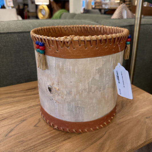 Decorative pot with leather trim and tassels on a wooden surface