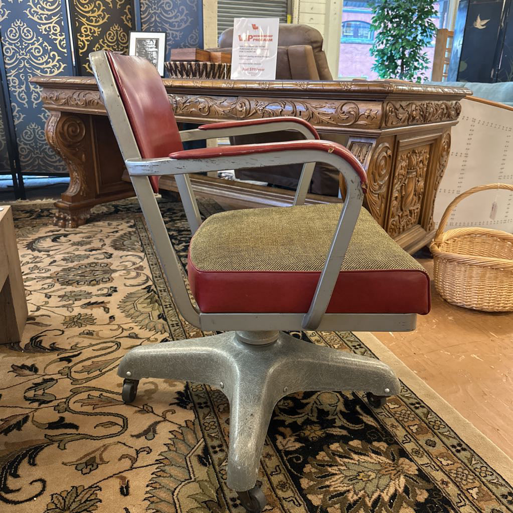 Vintage office chair with red cushioned seat and backrest in a room with patterned carpet and decorative elements.