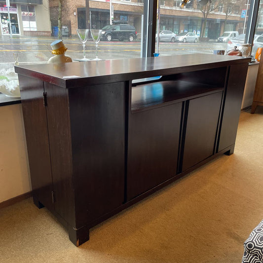 Dark wooden bar counter with a reflective surface in a room with large windows.