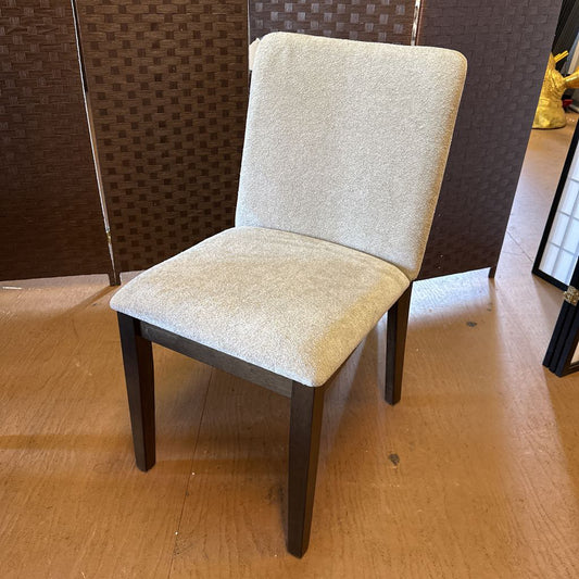 Beige upholstered chair with dark wooden legs on a wooden floor.