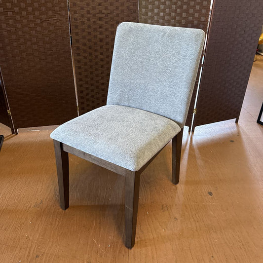 Gray upholstered chair on a wooden floor with a patterned wall in the background