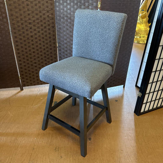 Gray cushioned chair on a wooden floor with a textured wall in the background