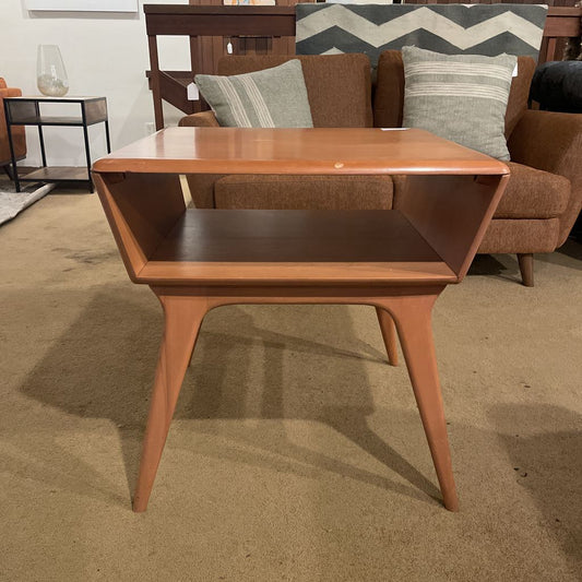 Wooden side table in a room with a sofa and decorative pillows.