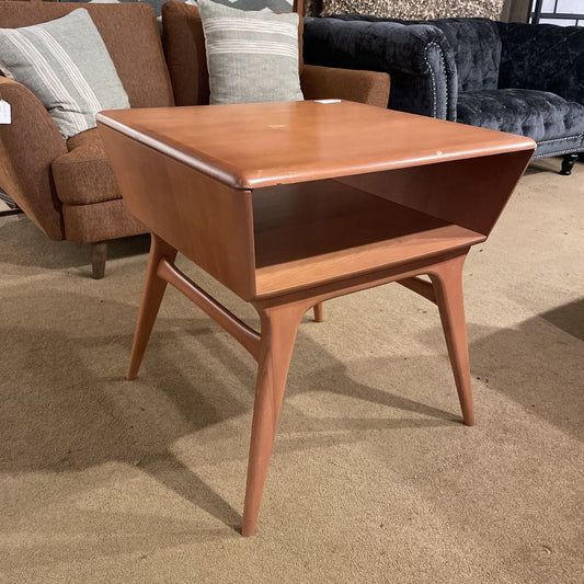 Wooden side table in a room with furniture including a sofa and armchair.