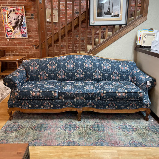 Floral-patterned sofa in a room with a brick wall and staircase.