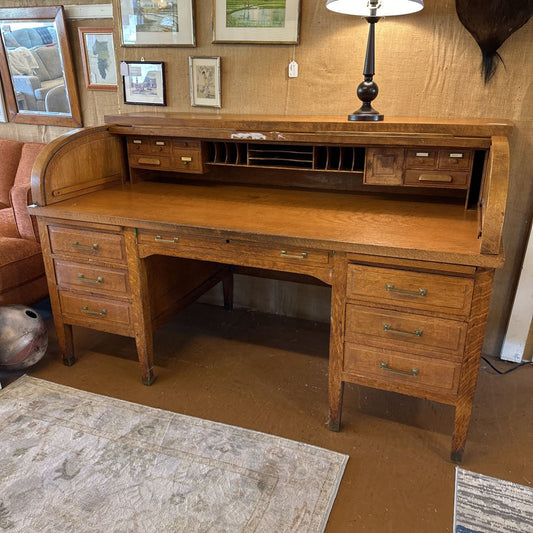 Wooden roll-top desk in a room with framed pictures on the wall.