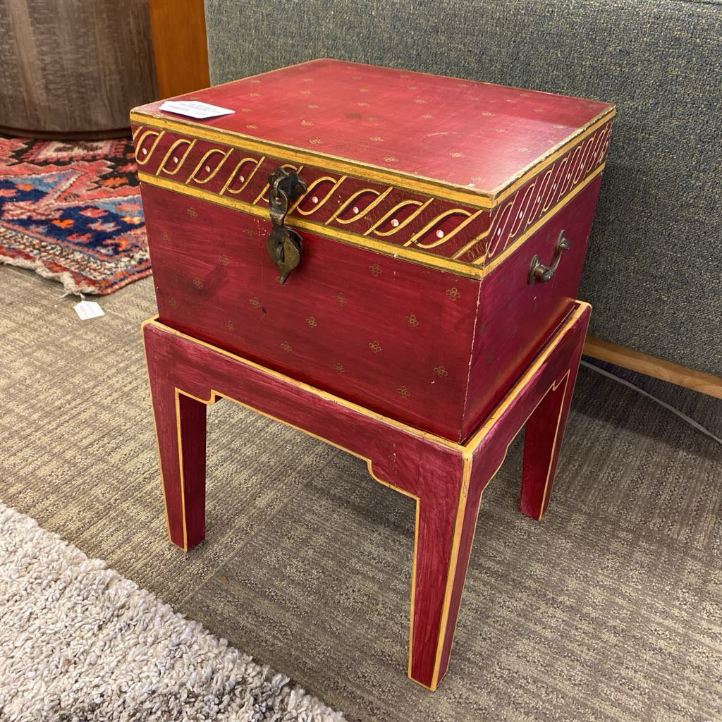Red wooden side table with gold accents on a carpeted floor.