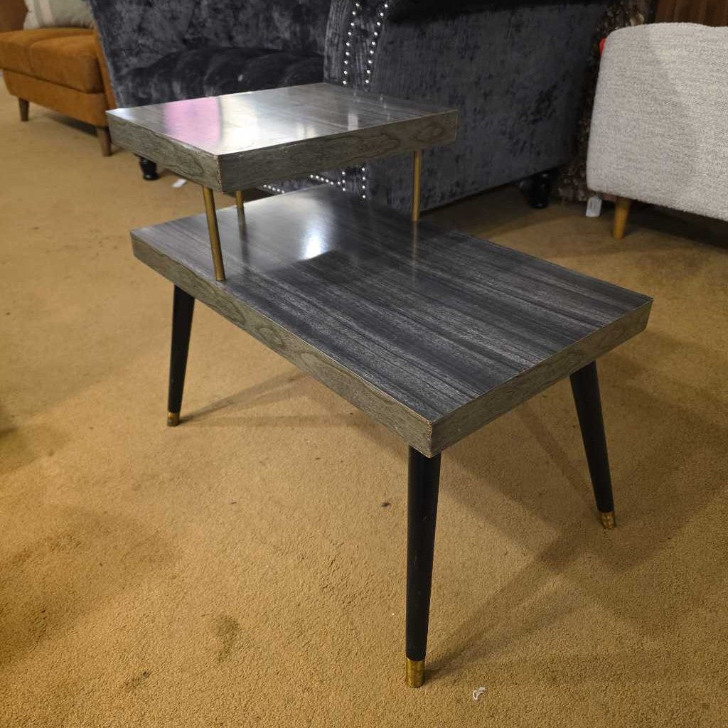 Two-tiered metal table on a carpeted floor with furniture in the background