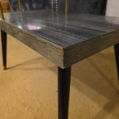 Close-up of a wooden table with black metal legs on a wooden floor.