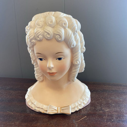 White ceramic bust of a woman with decorative hair on a wooden surface