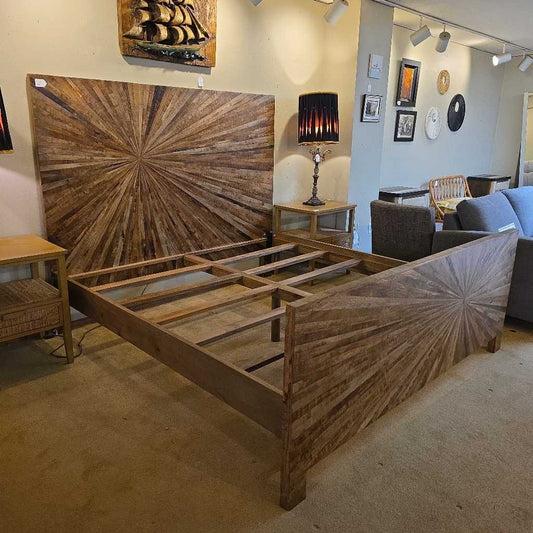 Wooden bed frame with starburst design headboard in a room setting.