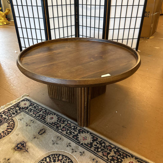Wooden round table in a room with a rug and a black metal screen.