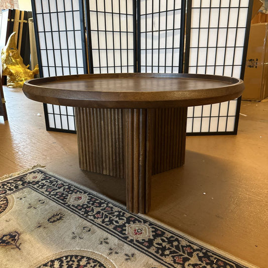 Wooden round table in a room with a decorative rug and black screen.
