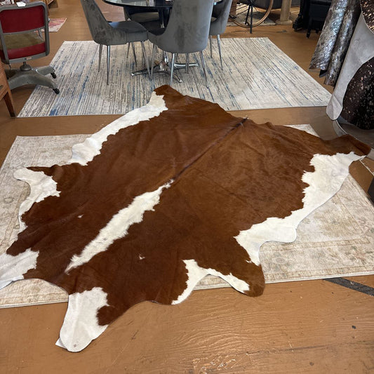 Brown and white cowhide rug on a wooden floor with a room in the background
