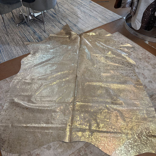 Gold metallic fabric on a table with a textured floor and chairs in the background