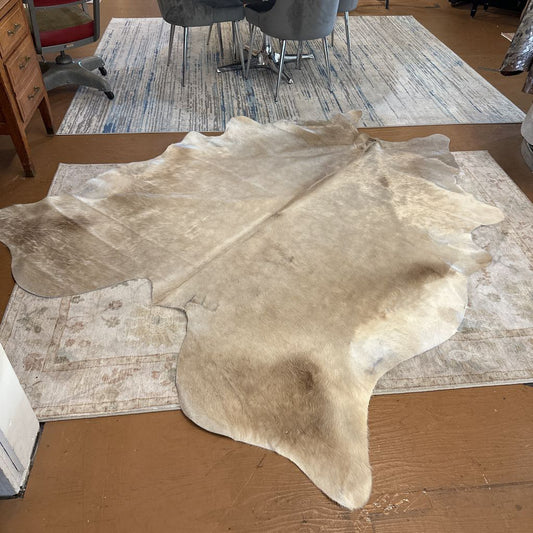 Beige cowhide rug on a wooden floor with a room in the background