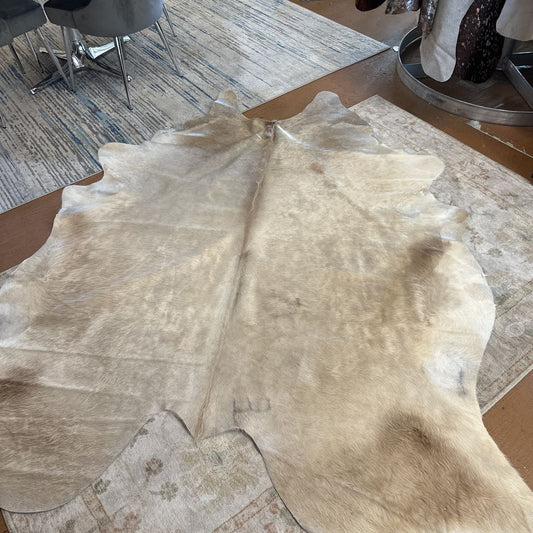 Cowhide rug on a wooden floor with chairs and a rug in the background