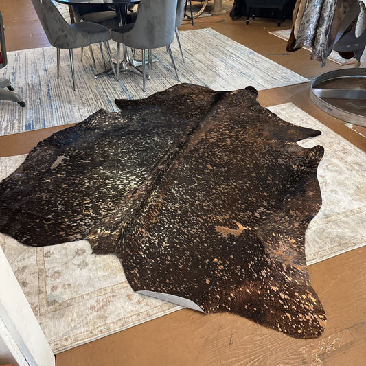 Brown cowhide rug on a patterned rug with a dining area in the background