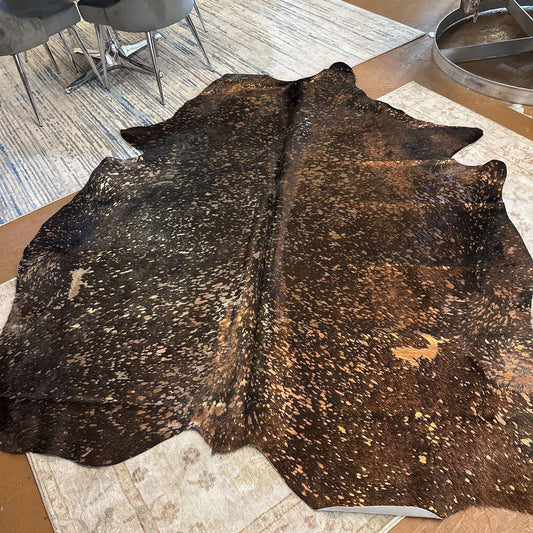 Brown cowhide rug on a patterned rug with a dining area in the background