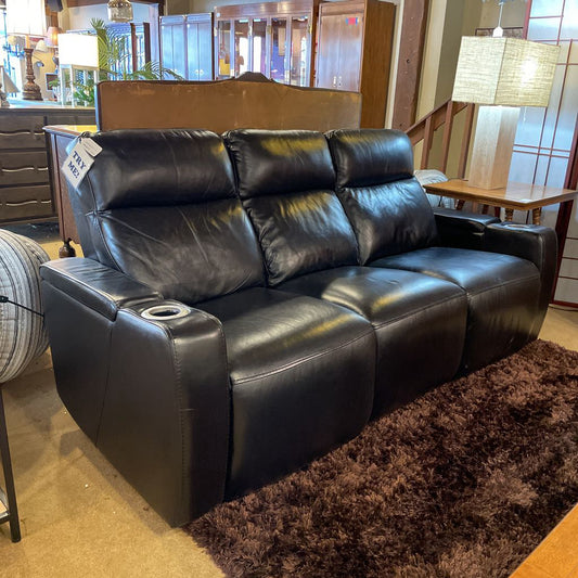 Black leather reclining sofa in a showroom setting with lamps and furniture.