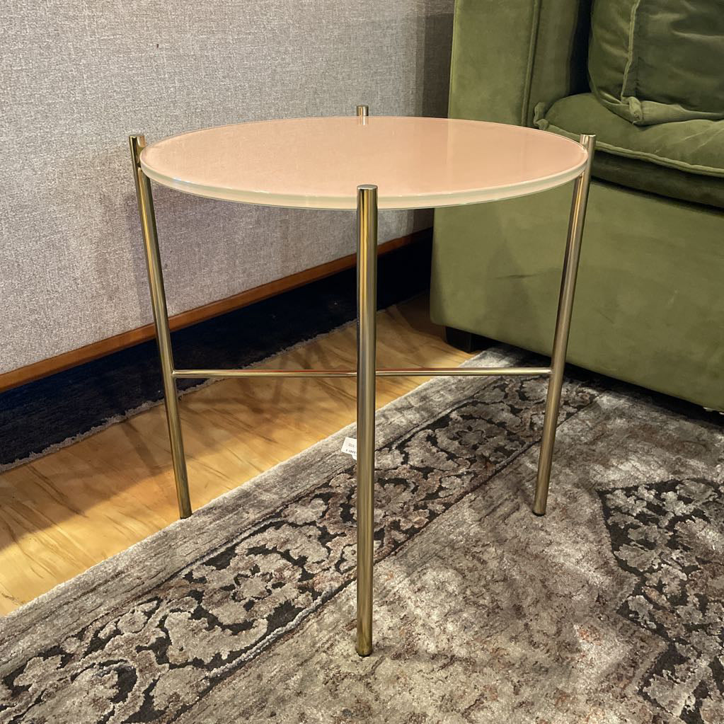 Small round table with gold legs on a patterned rug next to a green sofa.