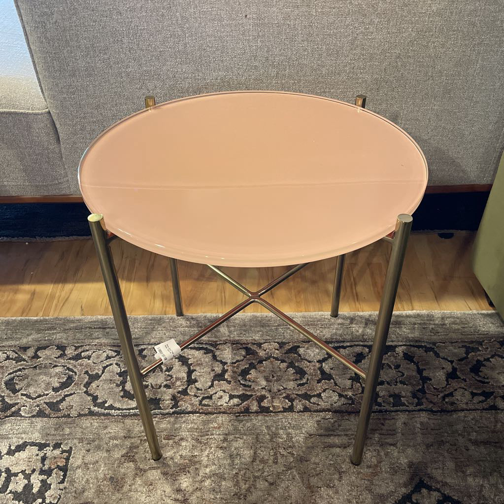 Small round table with a beige top and gold legs on a patterned rug.
