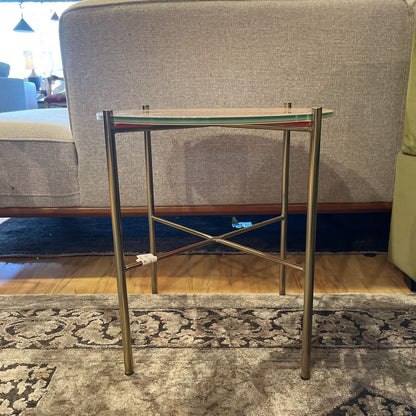 Small glass table with brass legs on a patterned rug in a room setting.