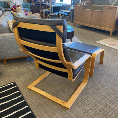Modern chair with wooden frame and black cushion in a room with furniture and decor.