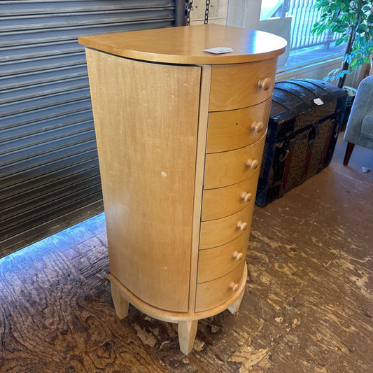 Wooden jewelry cabinet with multiple drawers on a carpeted floor.