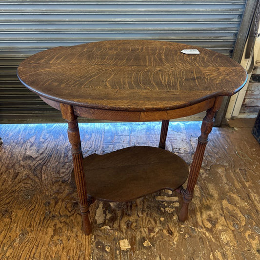 Wooden side table with scalloped edge on a wooden floor.