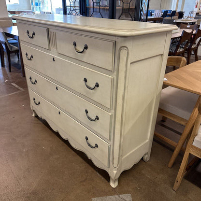 White dresser with multiple drawers in a room with tables and chairs.